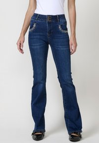 Jeans de mezclilla azul acampanados con cintura alta, costuras decorativas en los bolsillos y cierre de botones en la parte delantera. La textura del tejido es suave y ligeramente descolorida.