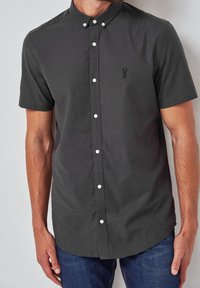 Camisa de botones de manga corta en color carbón con collar, botones blancos y un pequeño logo negro en el pecho. Tejido suave y ligero.