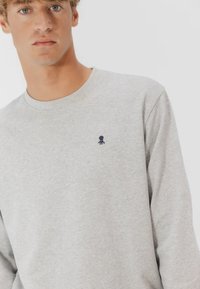 Felpa grigia in cotone, con maniche lunghe e scollo tondo. Piccolo logo di un polpo navy sul petto sinistro. Tessuto liscio.