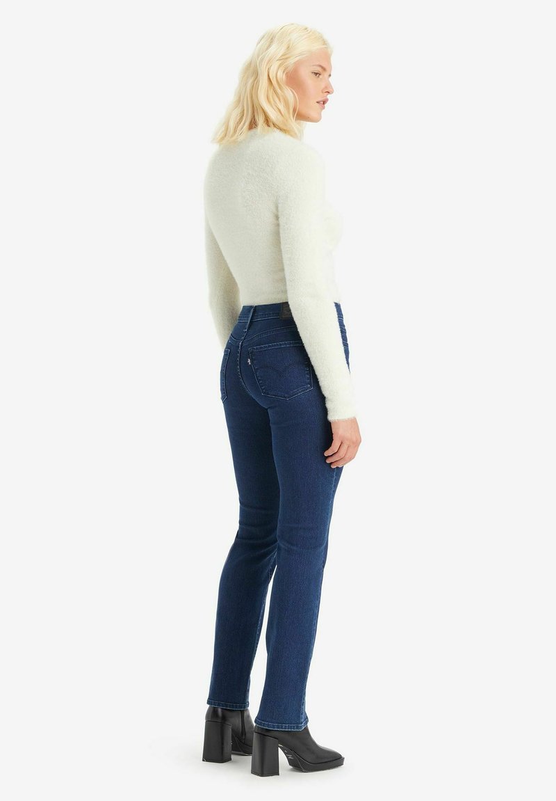 Maglione aderente color crema con maniche lunghe, abbinato a jeans a vita alta blu scuro e stivali neri con tacco a blocco. Tessuto testurizzato sul maglione.