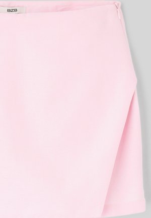 Jupe en tissu rose clair avec une fente latérale et une petite étiquette blanche près de la ceinture sur un fond gris.