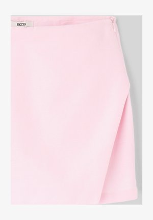 Jupe en tissu rose clair avec une fente latérale et une petite étiquette blanche près de la ceinture sur un fond gris.