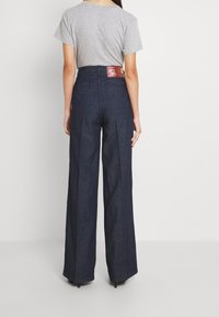 Högmidjade, vida jeans i mörk denim. Har en texturerad yta, bakfickor och en kontrasterande varumärkesetikett vid midjan.