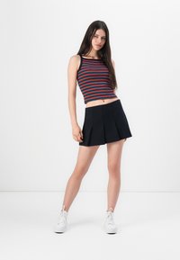 Jupe mini plissée noire associée à un crop top rayé multicolore. Le haut présente une coupe ajustée avec un col rond et une texture côtelée.