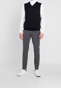 Schwarzer V-Ausschnitt-Pullover über einem weißen Rollkragenpullover, kombiniert mit schmalen grauen Hosen und weißen Sneakern. Einfaches, figurbetontes Design mit minimalen Akzenten.