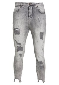 Jeans ajustados en denim gris claro con parches desgastados, dobladillos deshilachados y efectos de desgaste. Presenta un diseño clásico de cinco bolsillos y cierre de botón.