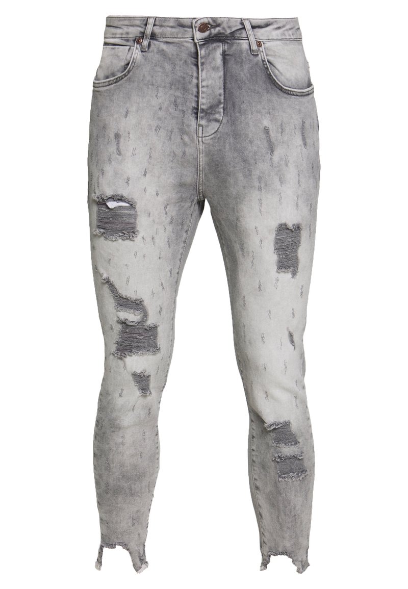 Jeans ajustados en denim gris claro con parches desgastados, dobladillos deshilachados y efectos de desgaste. Presenta un diseño clásico de cinco bolsillos y cierre de botón.