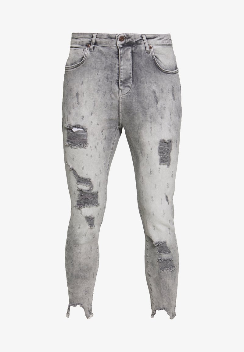 Jeans ajustados en denim gris claro con parches desgastados, dobladillos deshilachados y efectos de desgaste. Presenta un diseño clásico de cinco bolsillos y cierre de botón.