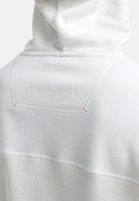 Witte hoodie met een gestructureerd onderste gedeelte, een soepel bovenmateriaal en een reliëfdetail "WEAR THE CODE" bij de hals.