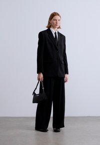 Μαύρο υπερμέγεθες σακάκι με ταιριαστό παντελόνι φαρδιάς γραμμής. Λευκό πουκάμισο και γραβάτα από κάτω. Μαύρη τσάντα χειρός με ασημένιες λεπτομέρειες, παπούτσια από πατίνιο.