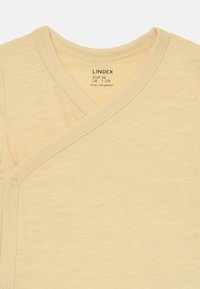 Bodysuit en coton jaune pour bébé, avec une partie avant croisée, fermeture à pressions et texture douce, étiqueté avec des informations sur la taille et l'entretien.