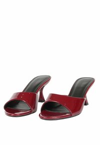Mule aperti in pelle patinata rossa con ampia fascia anteriore, tacco curvo e rivestimento interno nero, caratterizzati da una texture liscia e lucida.