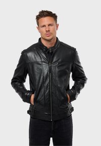 Chaqueta de cuero negro con cuello alto, detalles de costura visibles y cierre de cremallera. Presenta bolsillos laterales y una textura suave.