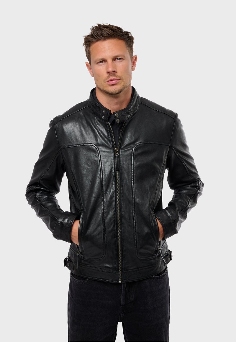 Chaqueta de cuero negro con cuello alto, detalles de costura visibles y cierre de cremallera. Presenta bolsillos laterales y una textura suave.