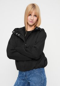 Μαύρο μπουφάν με κουκούλα, φερμουάρ μπροστά, κλείσιμο με κουμπιά και ελαστικά μανίκια, συνδυασμένο με μπλε τζιν με υφή. Απλός και λειτουργικός σχεδιασμός.