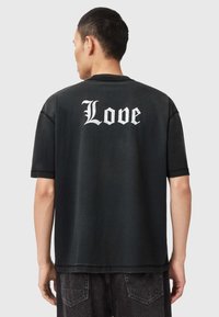 Fekete, túlméretezett póló nagy fehér "Love" grafikával a hátulján, rövid ujjak és laza fazon. Pamut anyag, sima textúrával.