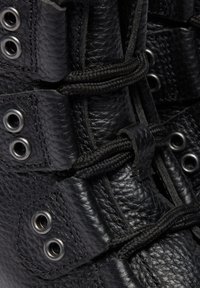 Gros plan sur une botte en cuir noir texturée avec des œillets métalliques et des lacets ronds noirs serrés passant à travers des boucles.