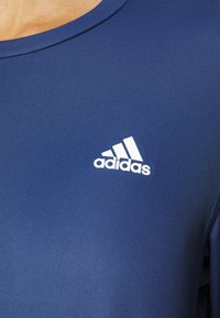 Marineblaues Sportshirt mit rundem Halsausschnitt, aus strukturiertem Stoff. Mit einem auffälligen weißen Adidas-Logo auf der linken Brustseite.