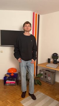 Sudadera negra con cuello redondo, jeans de color azul claro y zapatos marrones. La sudadera presenta un pequeño logo en el pecho.