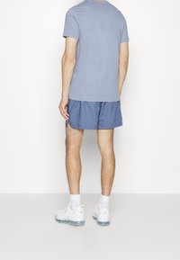 Herraktivkläder: ljusblå t-shirt med rund halsringning, marinblå shorts, vita löparskor med genomskinliga sulor, korta vita strumpor, sedd bakifrån.