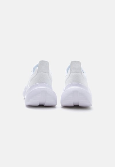 Paire de chaussures de sport blanches à semelles épaisses, vues de dos sur un fond clair uni.