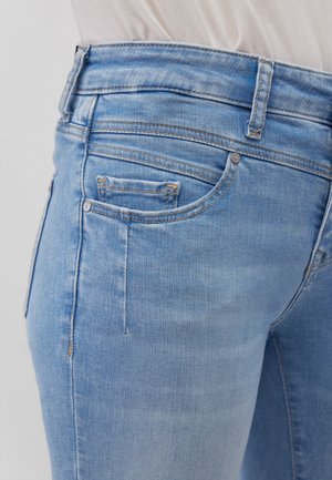 Nahaufnahme von hellblauen Jeans, die die Vordertasche, die Münztasche, die Gürtelschlaufen und die hellen Nähdetails vor einem weißen Hintergrund zeigen.