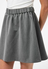 Gonna svasata grigia realizzata in tessuto morbido, con una vita elastica arricciata e una superficie liscia, che arriva a metà coscia.