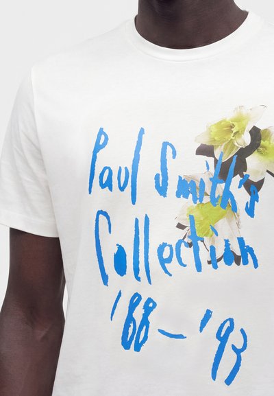 Λευκό T-shirt με μπλε χειρόγραφο κείμενο "Paul Smith’s Collection '88 - '93" και πράσινο και λευκό λουλουδάτο σχέδιο στο στήθος.