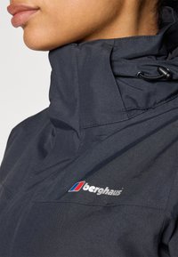 Námornícka bunda Berghaus s vysokým golierom, zipsovým zapínaním a nastaviteľnou šnúrkou. Obsahuje logo s červenými a modrými akcentmi na hrudi. Hladká textúra.