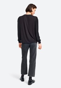 Zwarte longsleeve top met poffende schouders, gecombineerd met hoogopgetrokken donkergrijze rechte jeans en zwarte schoenen, gezien vanuit de achterkant.