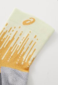 Chaussette montante avec un corps vert clair, un motif dégradé jaune et un talon gris. Fabriquée en tissu doux et texturé avec un détail de logo.
