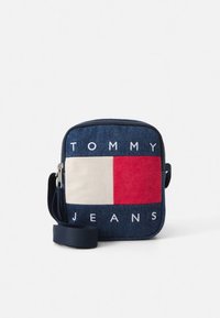Plava traper torbica preko tijela s prednjim dizajnom u obliku bijelog i crvenog pravokutnika. "TOMMY JEANS" ispisano bijelim slovima na dnu.