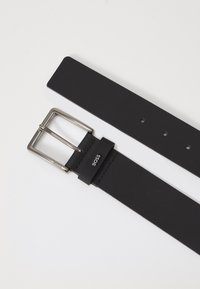 Zwarte leren riem met een zilveren rechthoekige gesp en een gebrandmerkte leren lus. Gladde textuur, minimalistisch ontwerp, meerdere aanpassingsgaten.