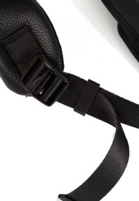 Mustekattu musta hihna, jossa on pehmustettu nahkakohta ja muovinen solki, kiinnitetty sileään, litteään hihnaan, joka osoittaa joustavuutta ja kestoa.