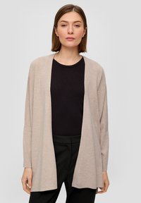 Beige open-front cardigan met lange mouwen. Zacht, lichtgewicht materiaal, rechte snit en verlaagde schouders. Gelaagd over een zwarte ribbed top.