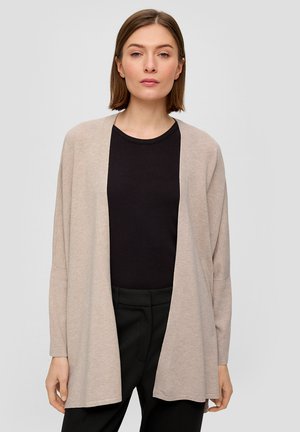 Cardigan beige à ouverture frontale avec des manches longues. Tissu doux et léger, coupe droite et épaules tombantes. Porté par-dessus un top noir côtelé.