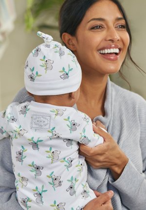 Un body et un bonnet pour bébé blancs avec des motifs de koala et des feuilles vertes. Tissu doux, col rond et une petite étiquette à l'arrière.