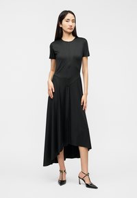 Μαύρο φόρεμα με κοντά μανίκια και ασύμμετρο τελείωμα, εφαρμοστό μπούστο, λείο ύφασμα και διακριτικές ραφές. Το μοντέλο συνδύασε με μυτερά τακούνια.