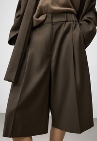 Brązowe spersonalizowane kuloty o teksturowanym wykończeniu, z szerokimi nogawkami, plisami i elastycznym pasem, w połączeniu z jasnobrązowym dzianinowym topem.