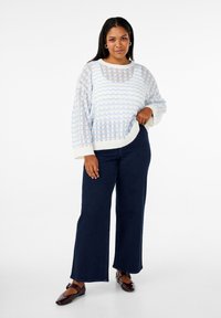 Pull en maille blanc et bleu clair avec un motif de vagues, coupe ample et manches larges. Associé à un pantalon large bleu foncé et des ballerines brunes.