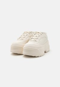 Füllige weiße Sneaker mit einem glatten Obermaterial aus Kunstleder, runder Zehenpartie, dickem strukturiertem Sohlen sowie Schnürsenkeln. Dezentes Branding auf der Zunge.
