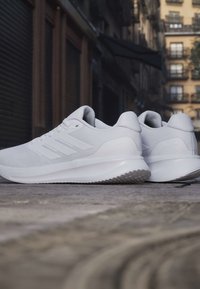 Paire de chaussures de sport blanches avec des semelles texturées placée sur une rue pavée dans un cadre urbain.