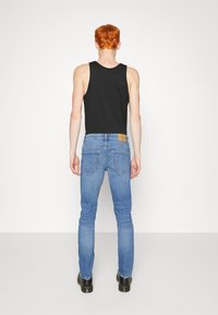 Svart ärmlös tanktop som matchas med ljusblå tajta jeans. Jeans har en brun läderlapp och en klassisk bakfickdesign.