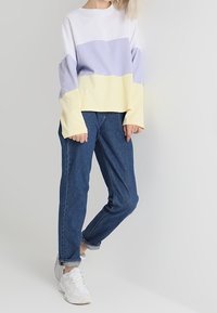 Bluza w kolorze białym, lawendowym i żółtym; miękki materiał, luźny krój. Połączona z niebieskimi dżinsami i białymi sneakersami.