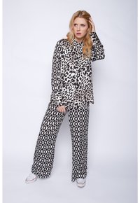 Schwarz-weißes Leopardenmusterhemd mit Kragen, kombiniert mit weit geschnittenen Hosen mit geometrischem Muster; das Model trägt weiße Sneakers.