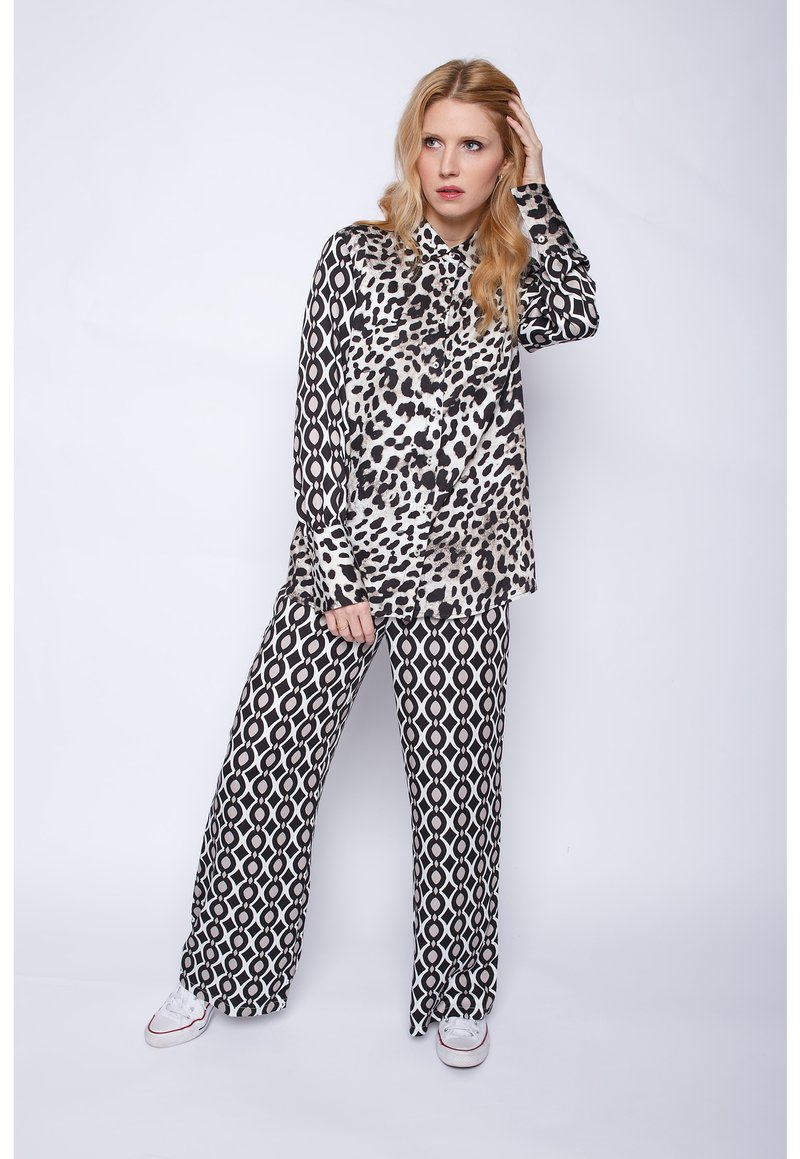 Schwarz-weißes Leopardenmusterhemd mit Kragen, kombiniert mit weit geschnittenen Hosen mit geometrischem Muster; das Model trägt weiße Sneakers.