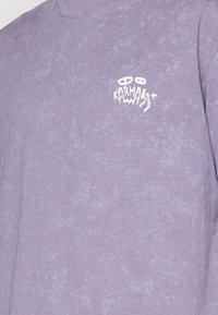 Lila Langarm-Sweatshirt mit einer subtilen Textur, das auf der Brust ein weißes grafisches Design mit dem Wort "KARMABOY" zeigt.