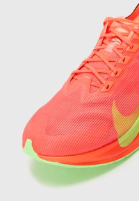 Bright orange running shoe with a textured mesh upper, featuring green accents on the sole and a pronounced toe cap for stability.
