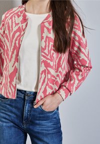 Zipjacka i rosa och krämfärgad abstrakt mönster. Vit T-shirt under. Bärs med blå denimjeans. Avslappnad passform med lång ärm.