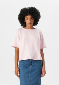 Rosa, teksturert, kortermet topp med rund hals og liten logo-detalj, kombinert med en denimskjørt.